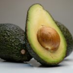 Nocciolo di avocado sorretto da stuzzicadenti sopra un bicchiere d'acqua trasparente.