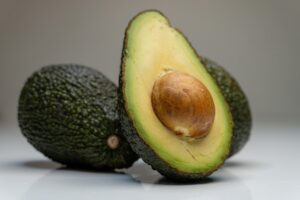 Nocciolo di avocado sorretto da stuzzicadenti sopra un bicchiere d'acqua trasparente.